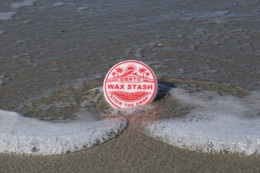 Red wax stash surf wax container on a beach with waves